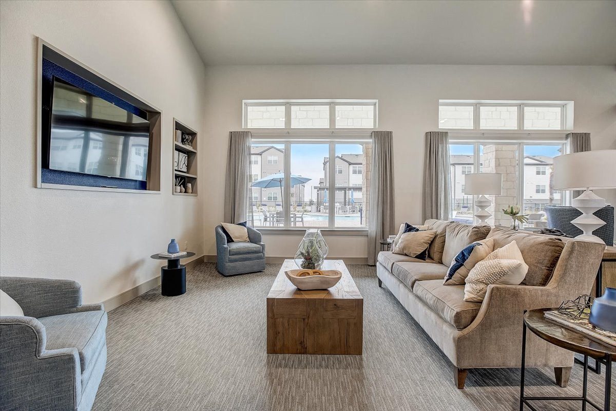 Community lounge with sofa seating, wall-mounted TV, and bright windows overlooking the courtyard.